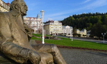 Bronzová socha muže sedícího na náměstí v Mariánských Lázních.