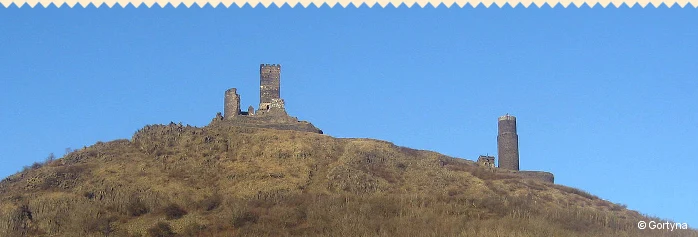 Zřícenina hradu na kopci s věžemi pod modrou oblohou.