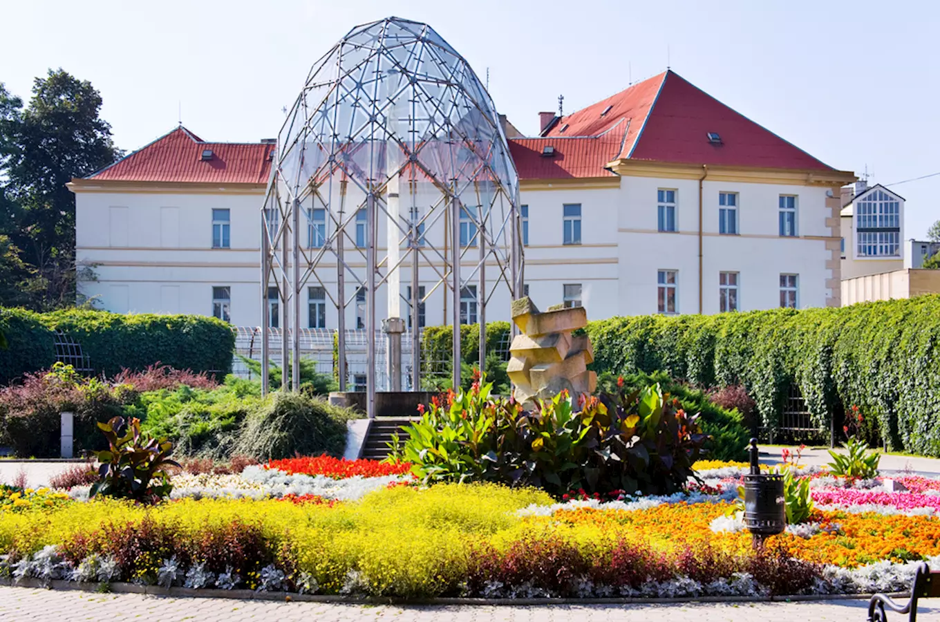 Skleněná kupole v zahradě před budovou s červenou střechou.