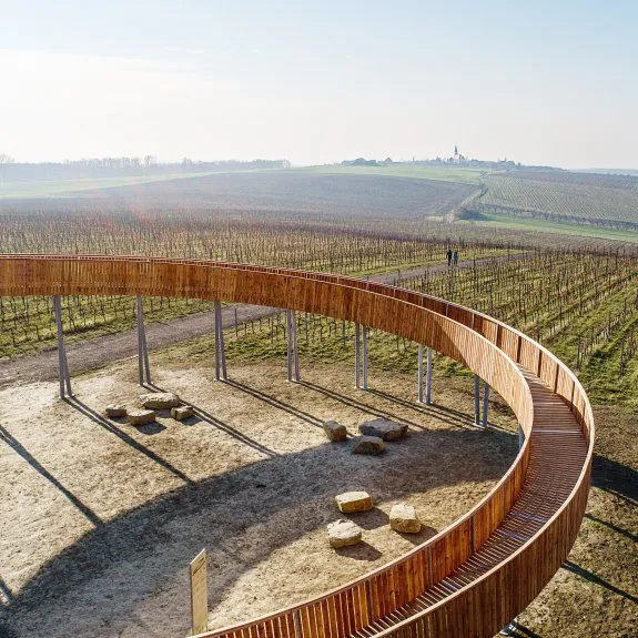 Dřevěná chodba nad vinicemi s výhledem na krajinnou panorámu.