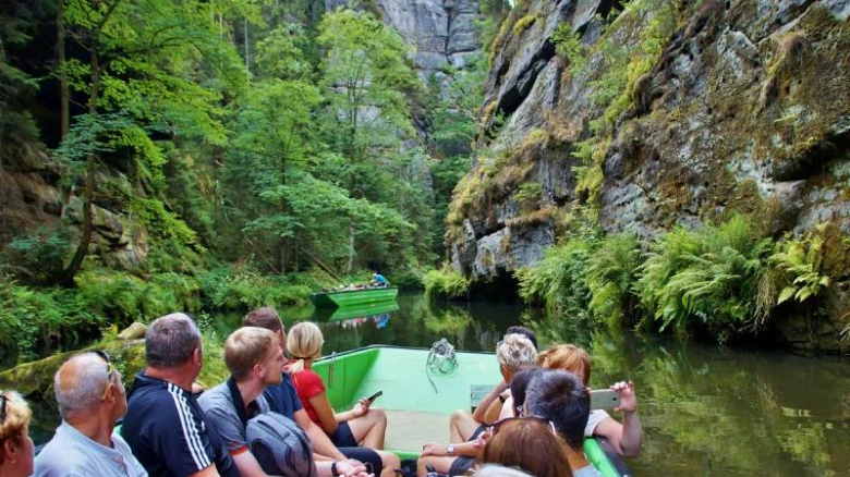 Turisté plují lodí po řece v úzkém skalním kaňonu.