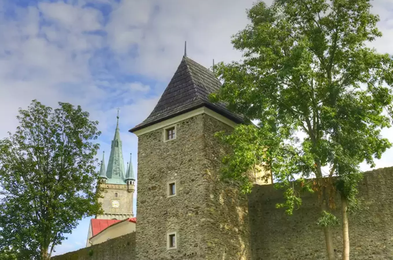 Zámek v Tachově s věží a kostelem na pozadí pod modrou oblohou.