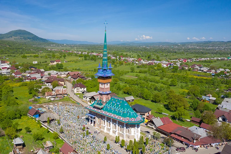 Kostel v Rumunsku s hřbitovem na pozadí zelené krajiny.