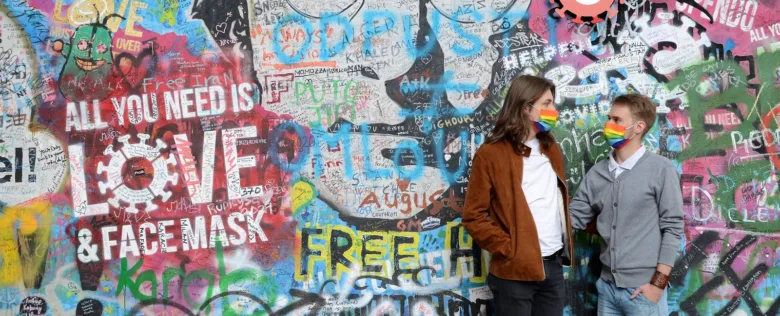 Dva lidé s deštníkovými maskami stojí před grafitovou zdí.