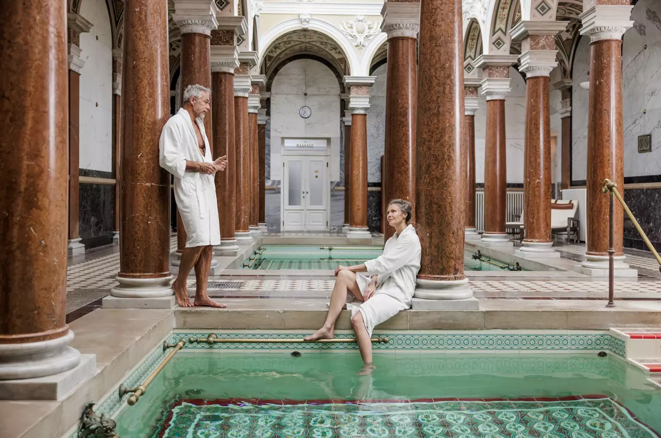 Muž a žena v koupacích pláštěch u bazénu ve wellness centru.