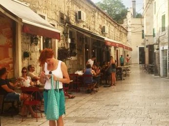 Žena stojí na ulici s venkovními kavárnami v Chorvatsku.