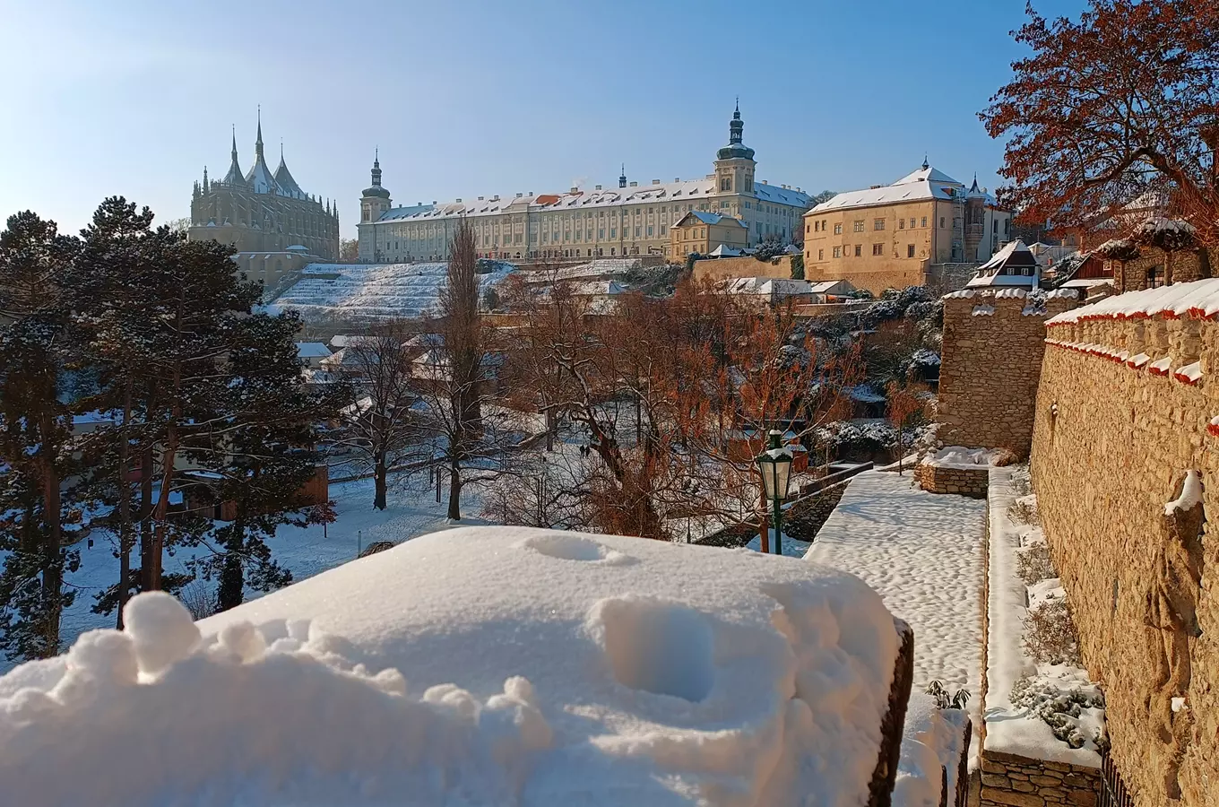 Zimní pohled na Pražský hrad s sněhem pod modrou oblohou.