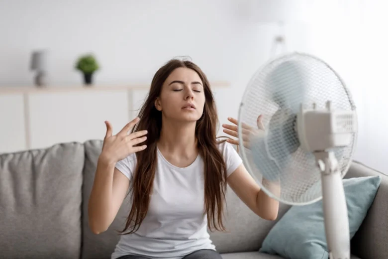Žena se ochlazuje ventilátorem při přehřívání v interiéru.