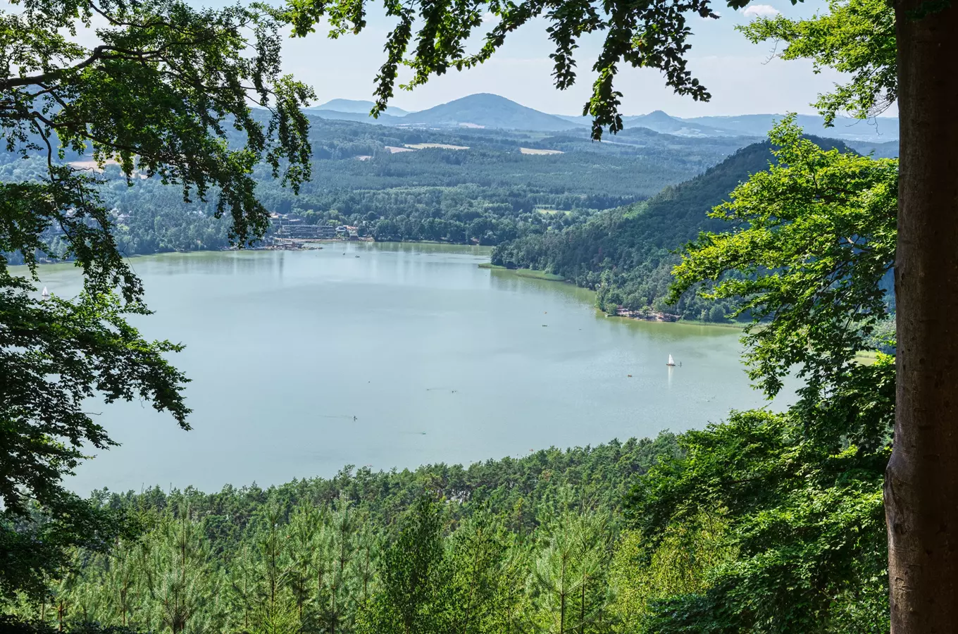 Pohled na jezero obklopené lesy a kopci.