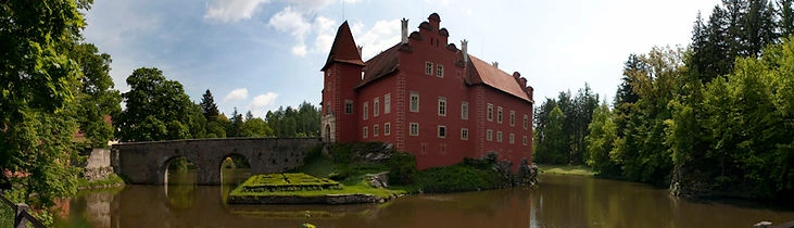 Zámek Červená Lhota obklopený vodou a zelenými stromy.