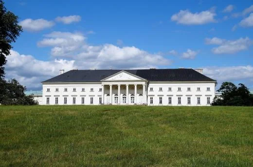 Exteriér zámku Kačiny na zelené trávě pod modrou oblohou.