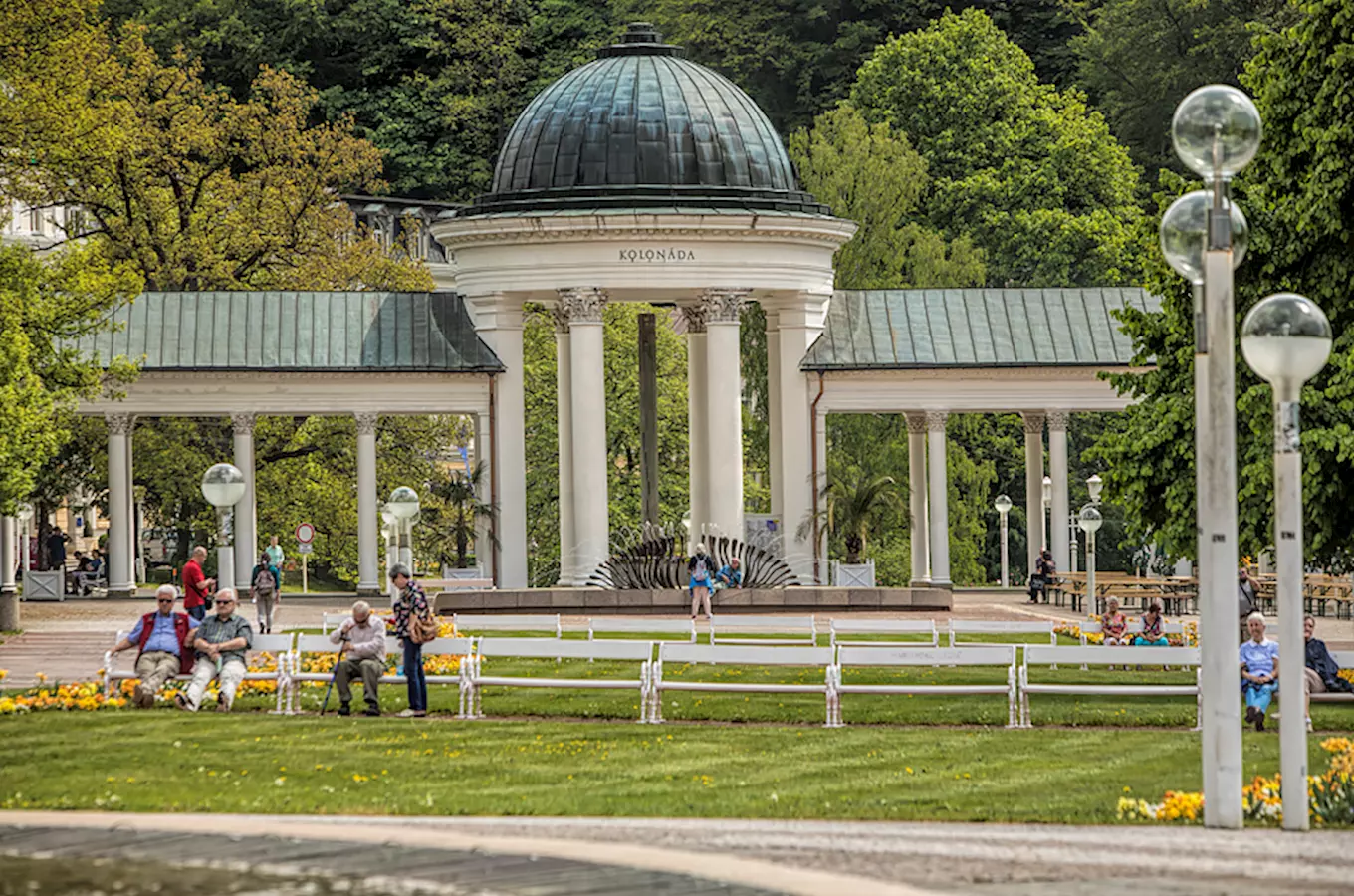 Pavilon Kolonáda v Mariánských Lázních s lidmi na lavičkách.