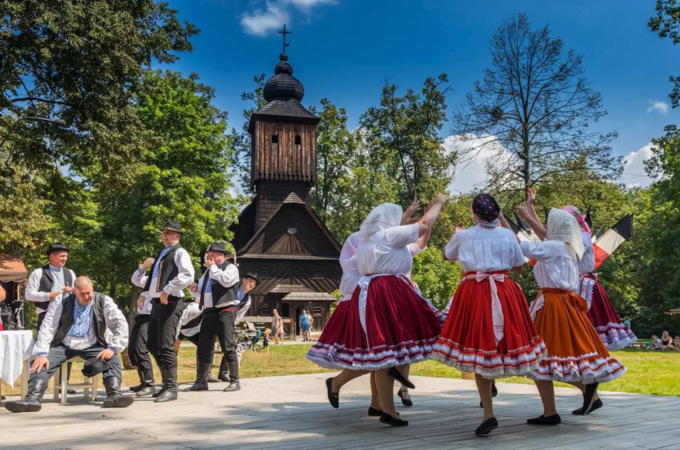 Tradiční taneční skupina před starou dřevěnou kostelem ve Zlínském kraji.
