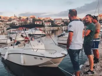 Muži u člunu na chorvatském přístavu s městem v pozadí.