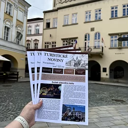 Ruka drží turistický průvodce v historickém náměstí Nového Jičína.