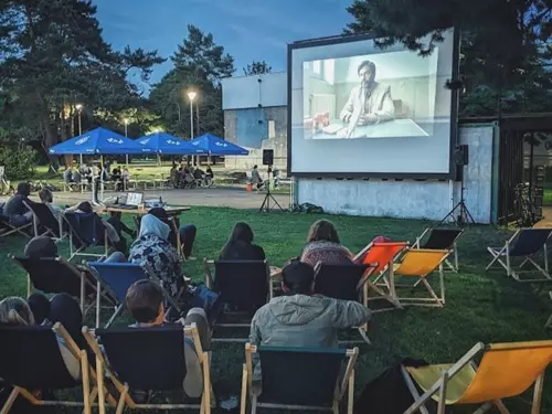 Venkovní promítání filmu na trávníku s diváky v křeslech.
