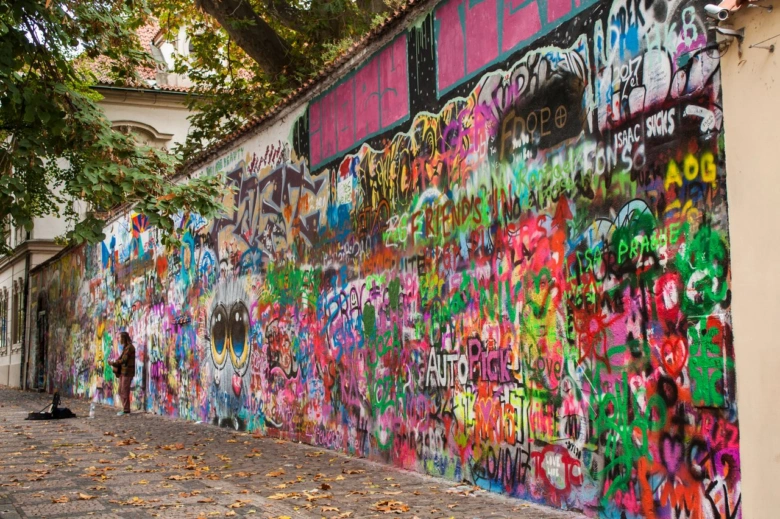 Lennonova zeď v Praze s barevnými graffiti a osobou u zdi.