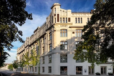 Historický hotel v Praze s elegantní fasádou mezi stromy.