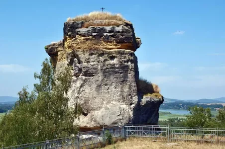 Velká skála s křížem na vrcholu v krajině u Doksech.