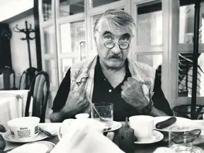 Český herec Pavel Landovský sedí za stolem v kavárně.