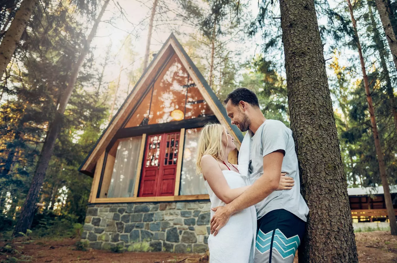 Manželé se objímají před chatou v lese pro romantický víkend.