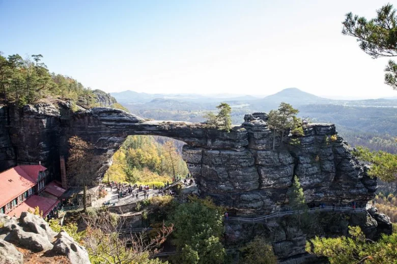 Přírodní most v Saském Švýcarsku s turistami na chodníčku.