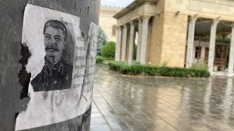 Plakát s portrétem Stalina na vlhkém sloupě před budovou.
