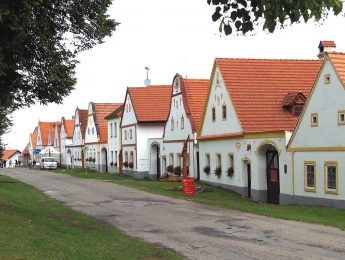 Řada bílých domů s červenými střechami v historické vesnici.