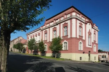 Historická budova v Hlinsku na klidné ulici s stromy.