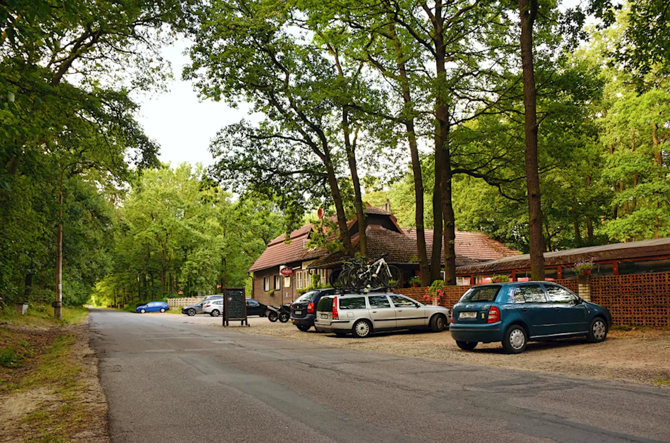 Parkoviště u restaurace v lesu s auty a bicykly.