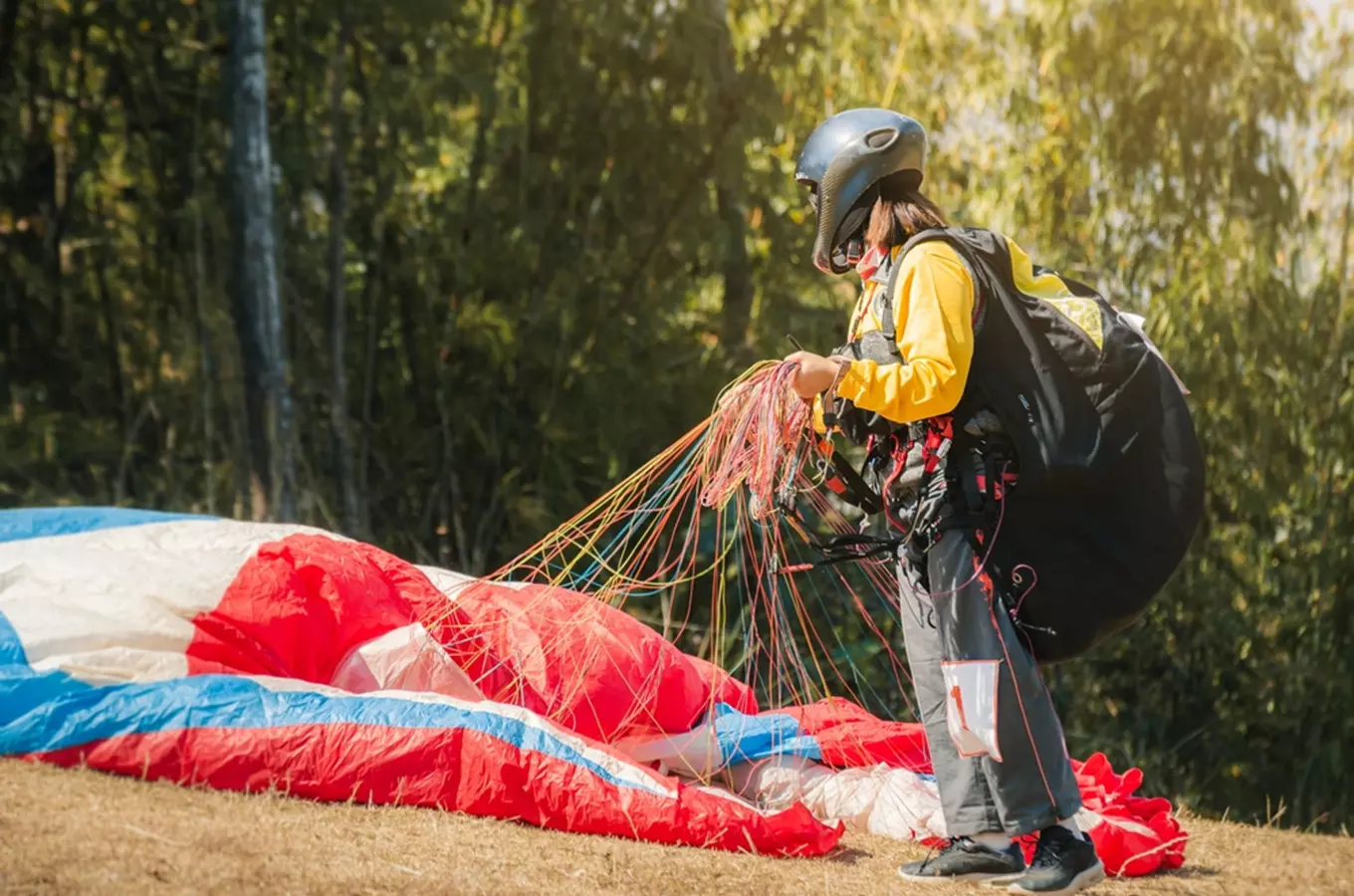 Člověk připravuje padák pro paraglidování na trávníku.