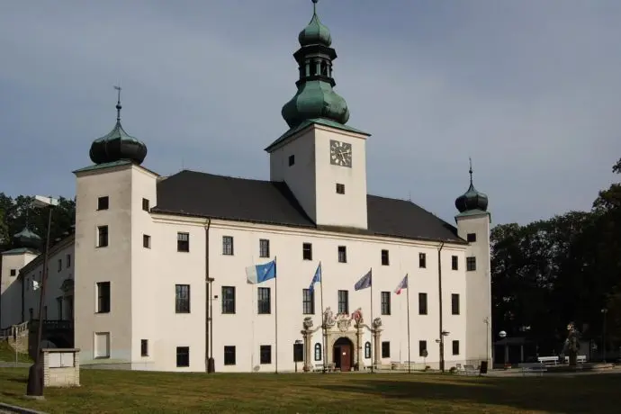 Bílá fasáda zámku v Telči s věží a zelenými kupolemi.