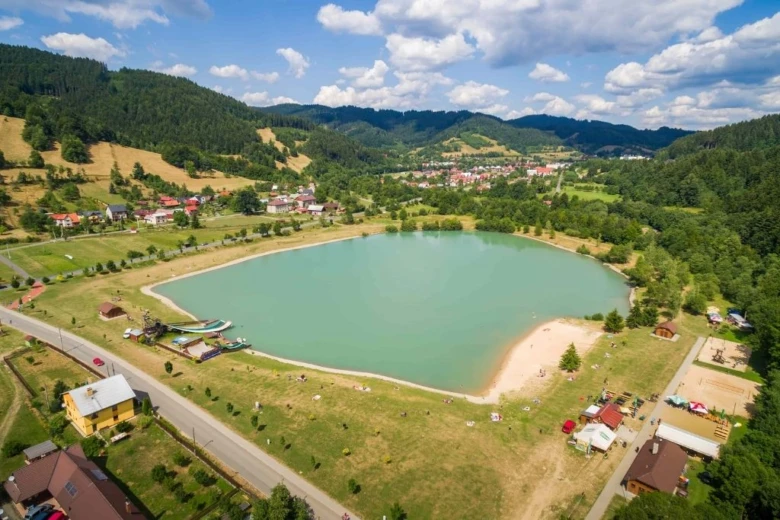 Pohled na jezero v horách s vesnicí a lesy.