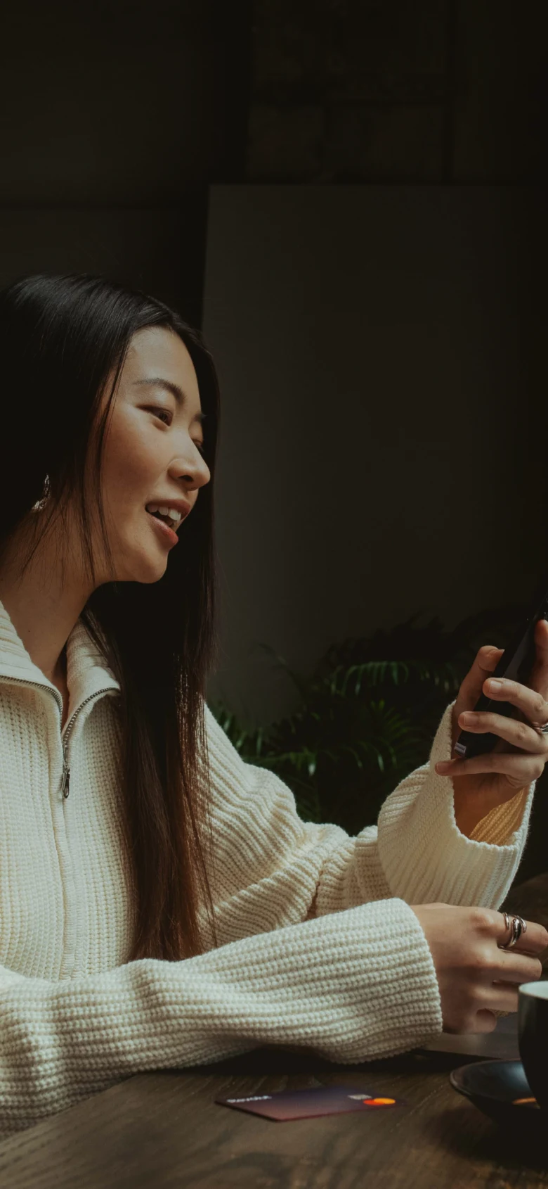 Žena se usmívá při používání mobilního telefonu v interiéru.