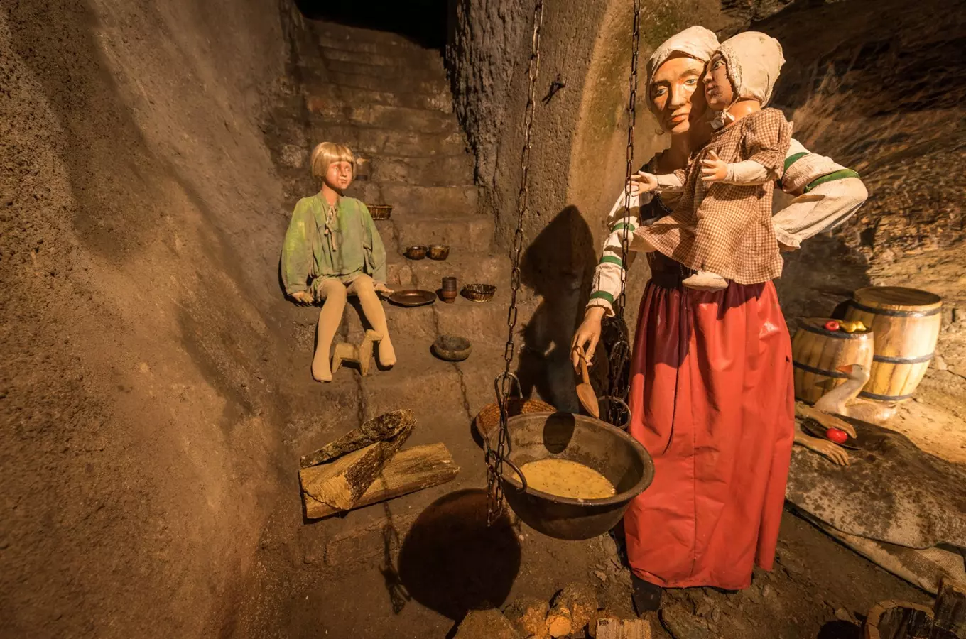 Historická scéna v podzemí s postavami vařícími u ohně.