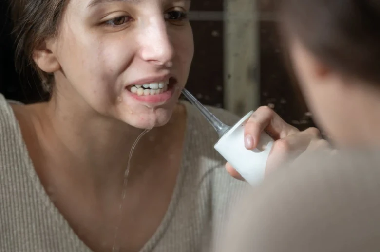 Žena používá ústní sprchu k čištění zubů v koupelně.