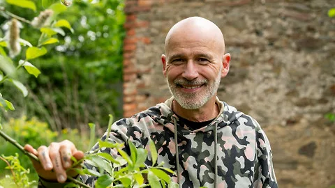 Muž v kamufláži drží rostlinu venku u zdi.
