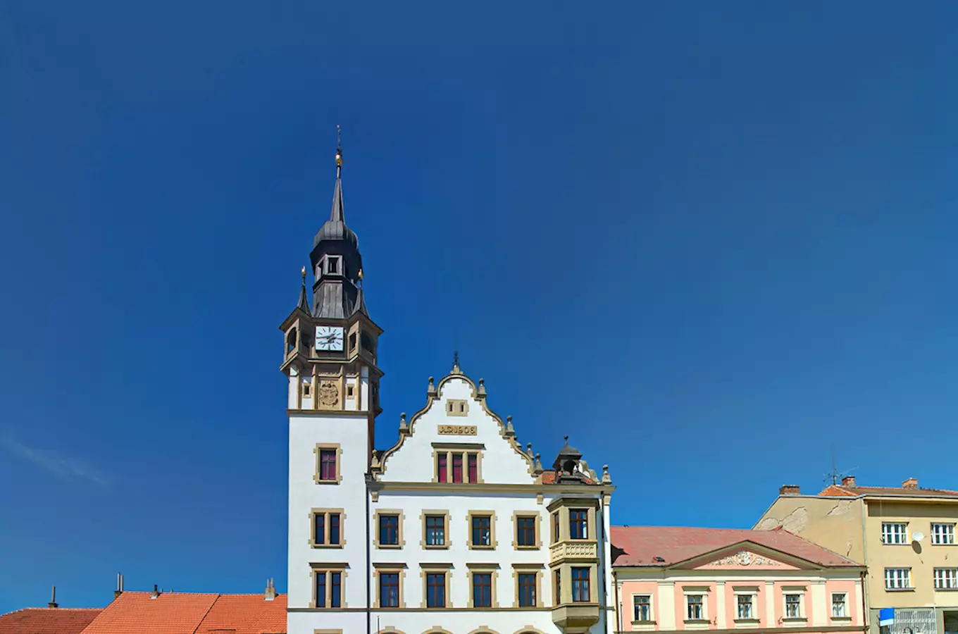 Zámek v Hustopečích s věží a hodinami na modré obloze.