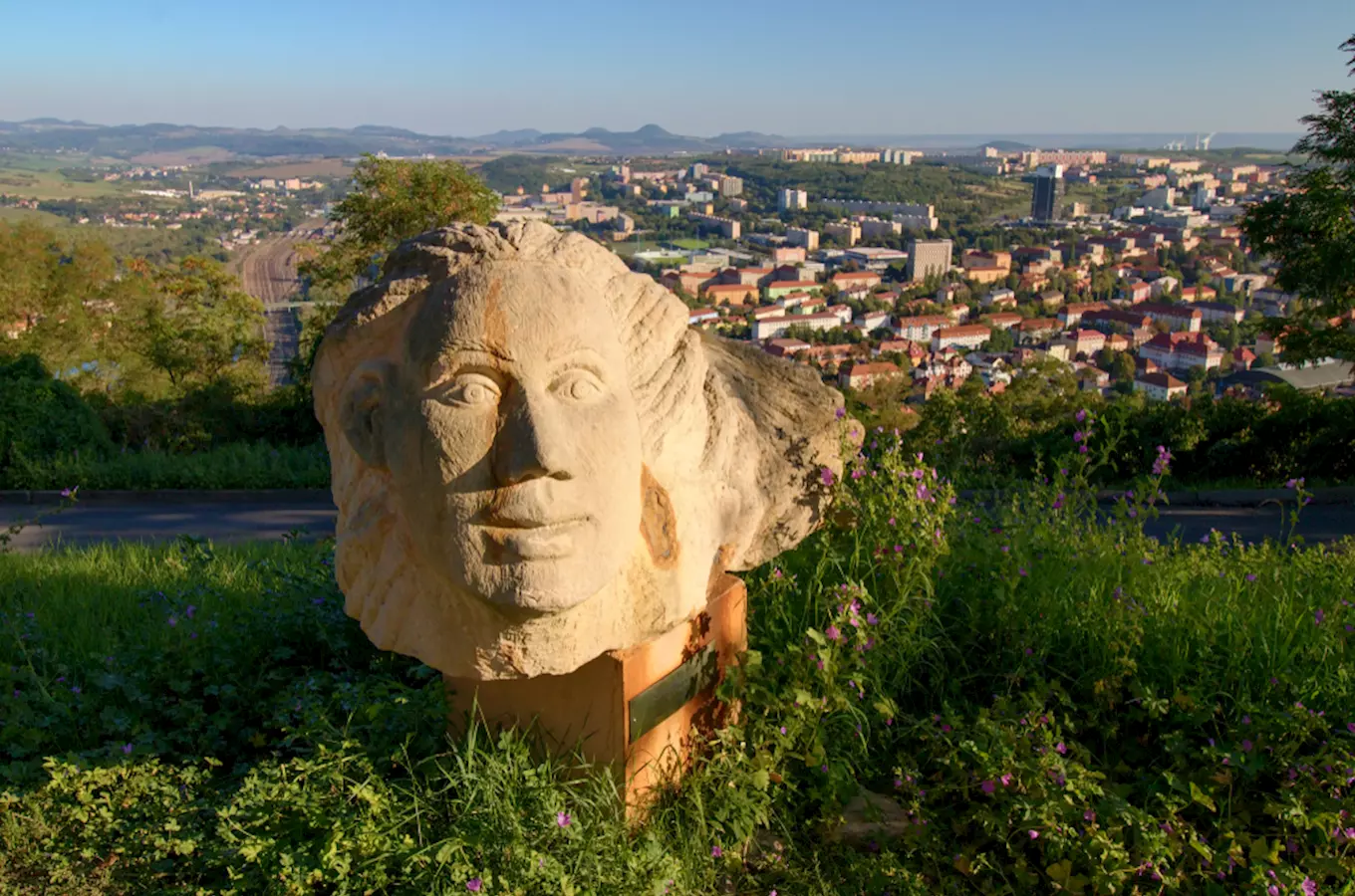 Kamenná socha hlavy s výhledem na město Most.