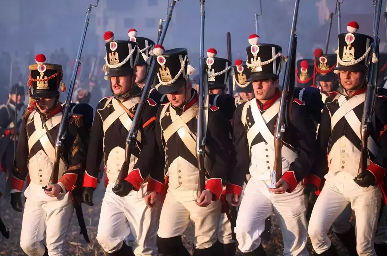 Reenaktoři v nábojích napoleonské armády pochodují s puškami.