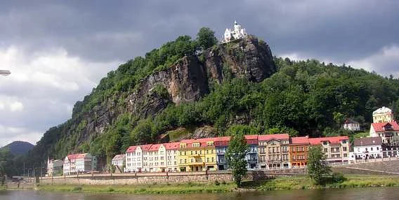 Zámek v Děčíně na skále nad řekou s barevnými domy.