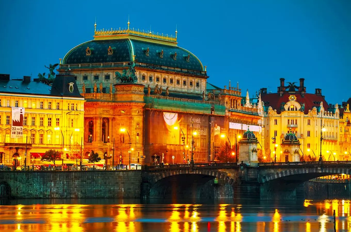 Státní opera v Praze osvětlená večerem s odrazem ve vodě.