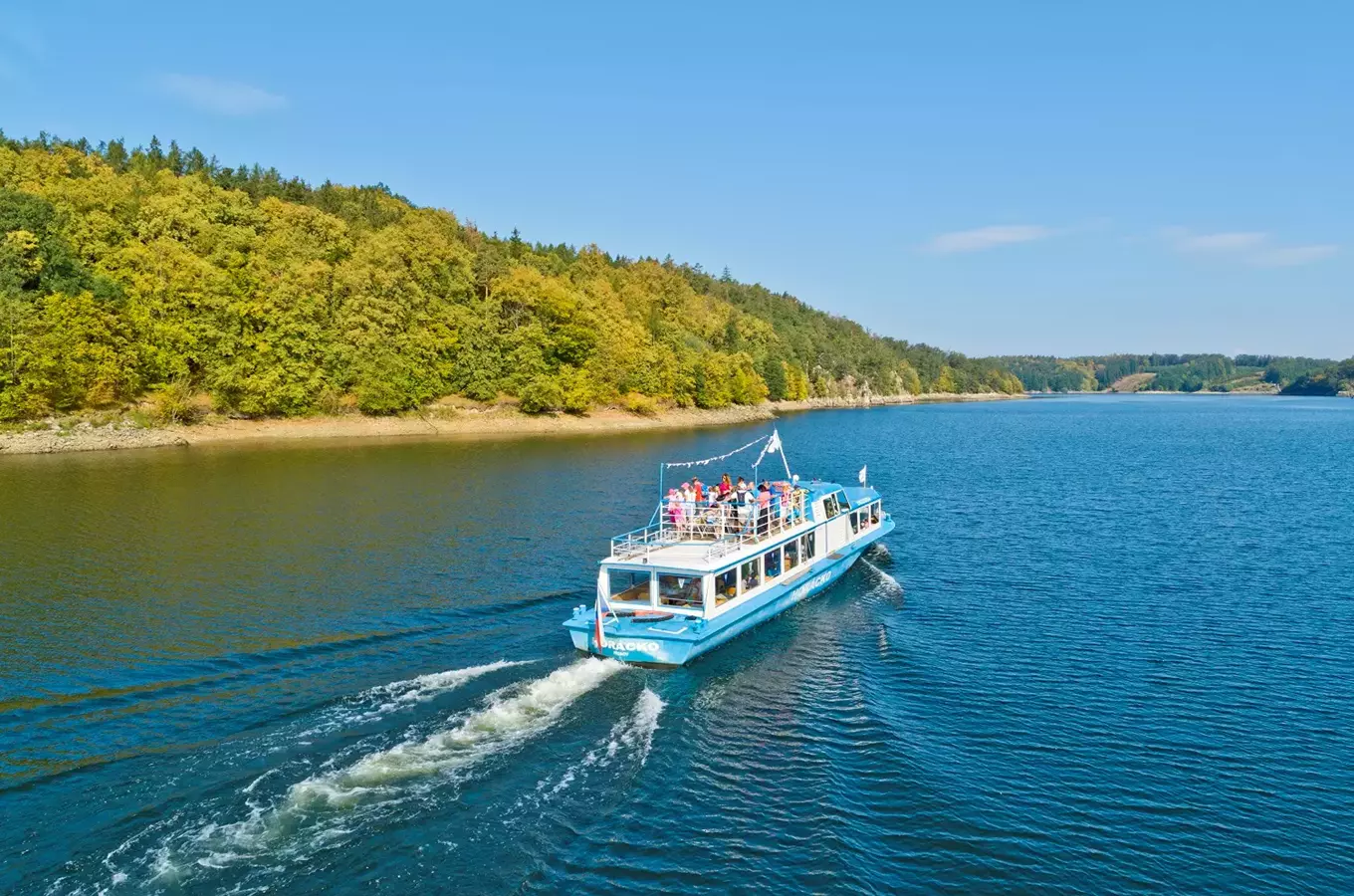 Modrá turistická loď pluje po jezeře s cestujícími na palubě.
