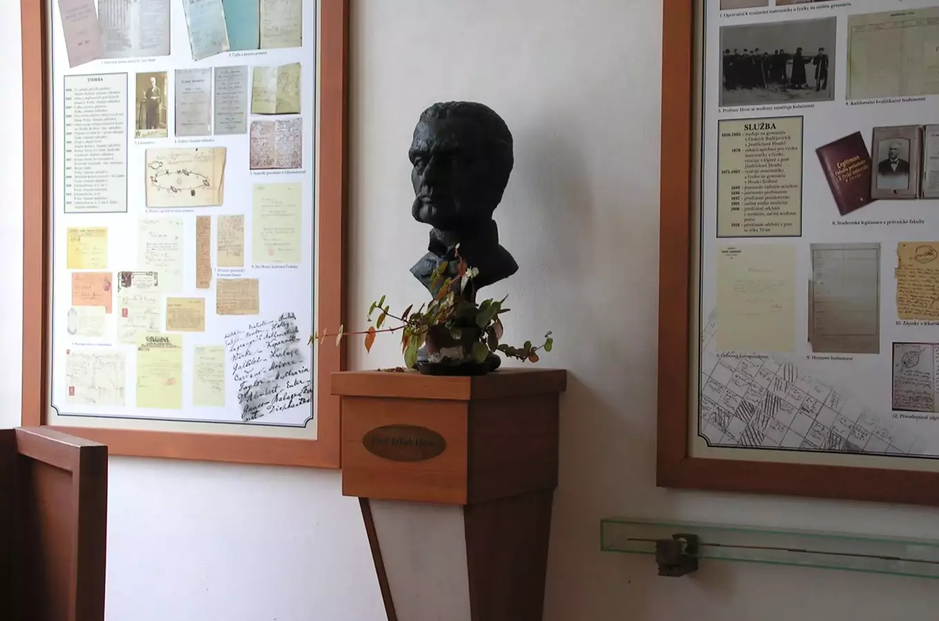 Socha na podstavci mezi dvěma rámy s historickými dokumenty.