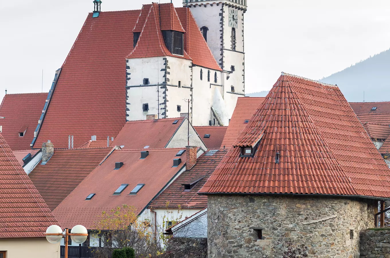 Historické střechy kostela svatého Jakuba v Pračaticích s kopcem na pozadí.