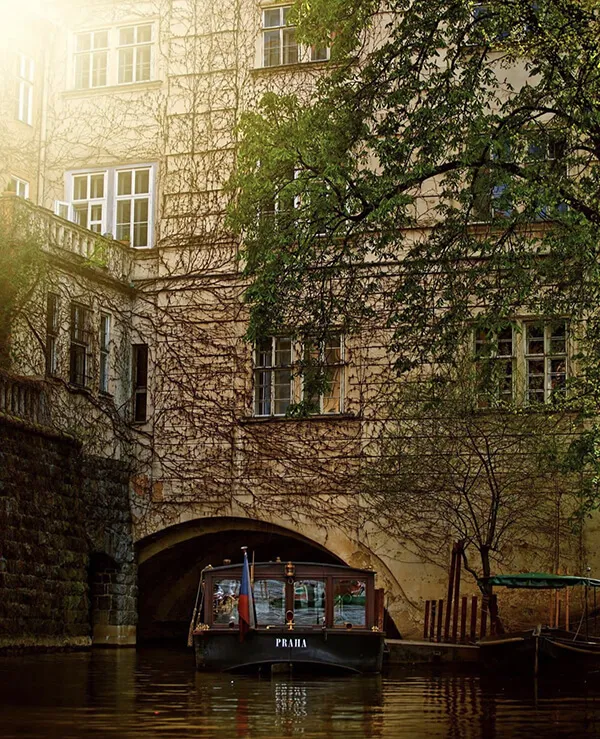 Turistická loď pluje pod mostem po historickém kanálu v Praze.