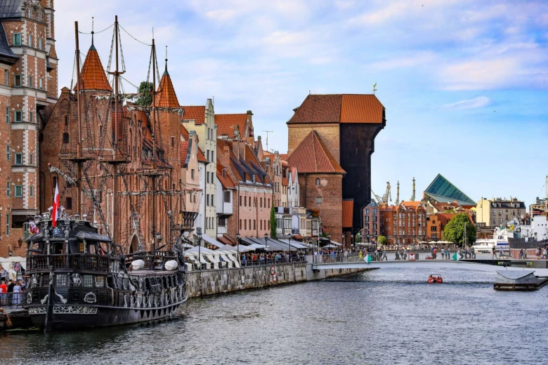Historické centrum Gdanska u řeky s loděmi na břehu.