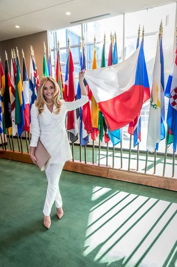 Žena v bílém obleku drží českou vlajku mezi mezinárodními vlajkami.