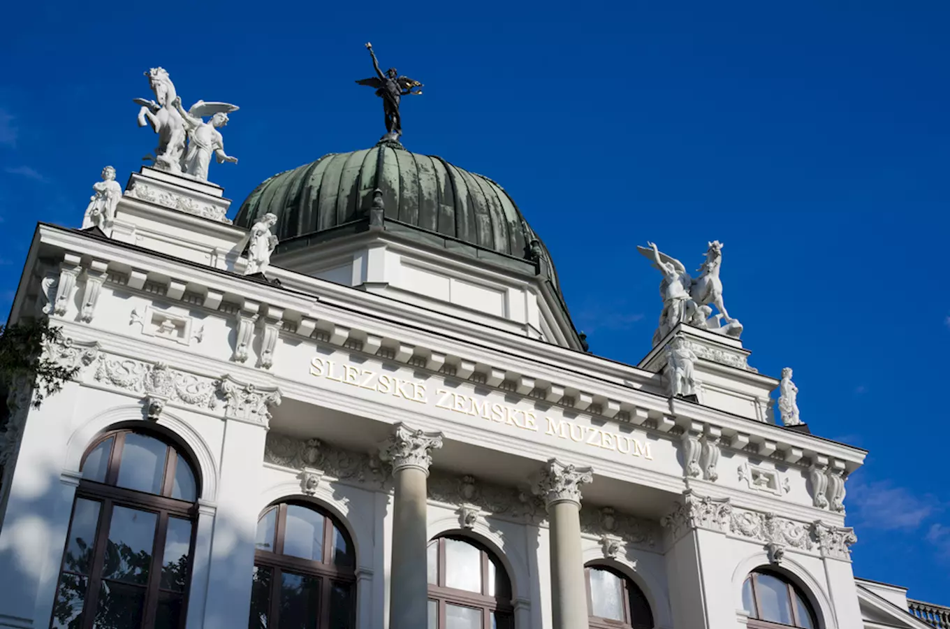 Fasáda Muzea zemského v Ostravě s sochami na střeše.