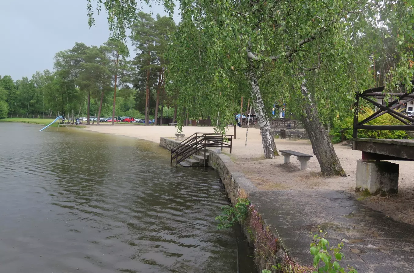 Koupaliště s písečnou pláží a stromy u jezera.